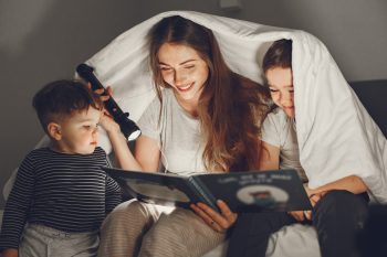 madre leyendo cuento a sus hijos en la cama bajo las sábanas momento de lectura en familia