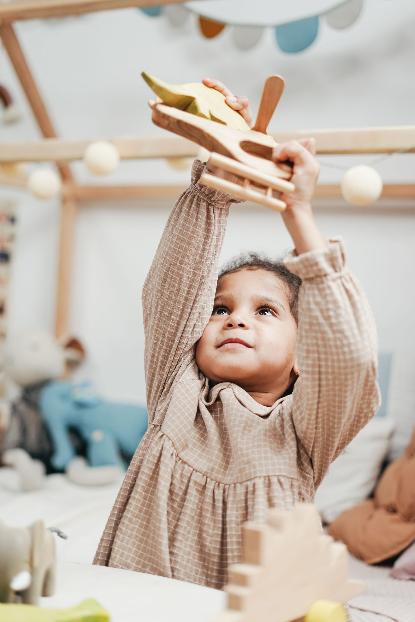 Niña de 4 años jugando con un avión de madera, ejemplo de juguete educativo que fomenta la imaginación y el juego libre.